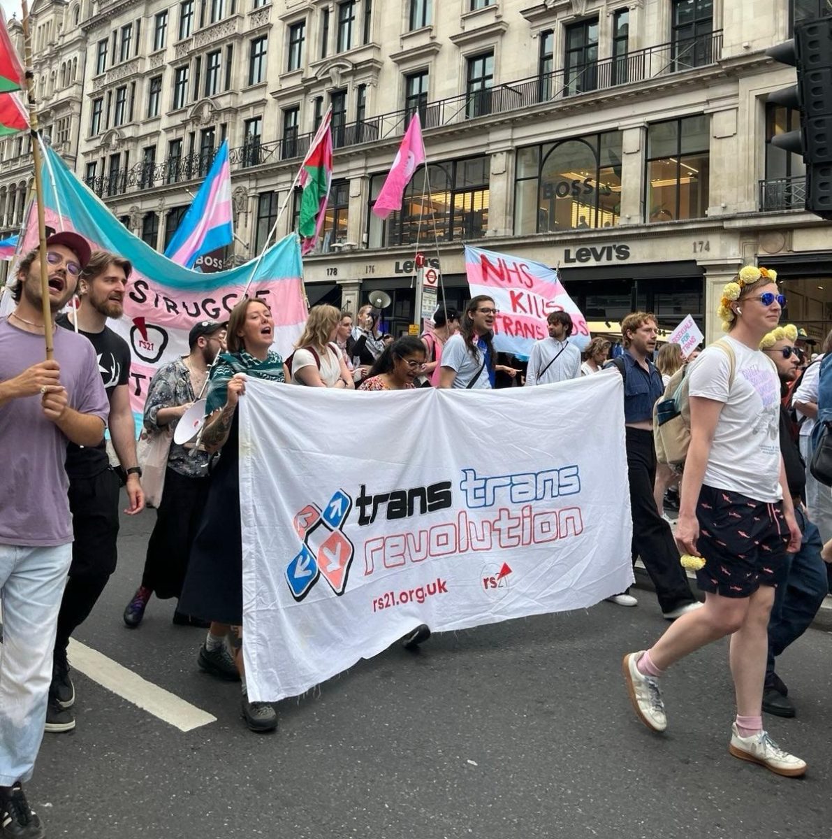 The rs21 bloc marches with a banner reading trans trans revolution