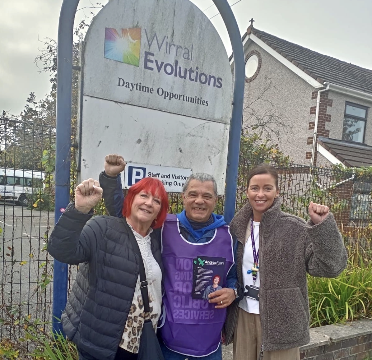 Andrea Again together with two striking workers on a picket - standing in front of of a sign saying Wirral Evolutions. All there have clenched fists.