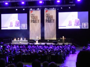 Long shot of the the conference hall stage two screens with blurred images of Corbyn and two long banners with slogan This is Your Party