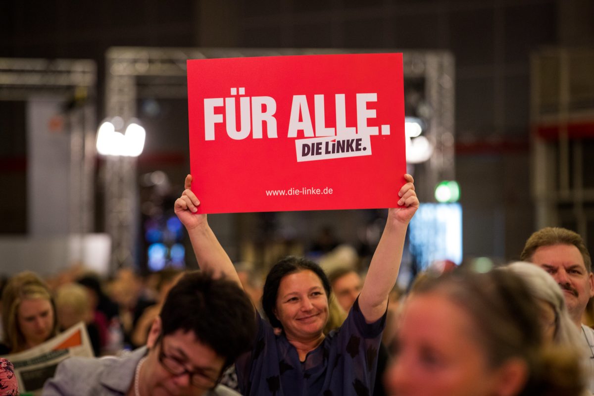 A photo from a Die Linke party congress. One party member smiles and holds a sign saying "For everyone. Die Linke" in German.