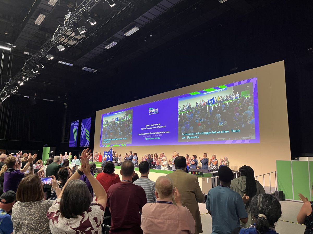 Delegates applaud at Unison conference with large screens in the background
